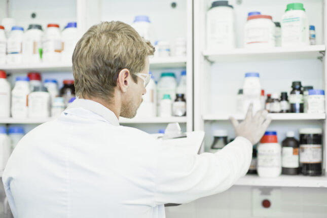 A laboratory scientist with a clipboard examines bottles of chemicals stored on shelves as part of an effective reagent management process