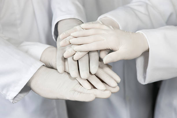 Scientists in lab coats and surgical gloves stack hands in a celebration of the resilience introduced by digitalizing quality control operations in their lab