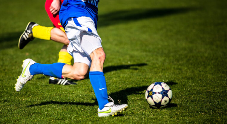 2 soccer players compete for a ball on a pitch. Soccer can provide some insights into how to improve QC planning adherence