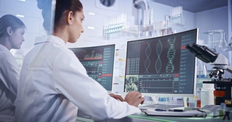 Scientists in white coats operate computers in a lab, illustrating the role of digitalization in biopharma process development labs
