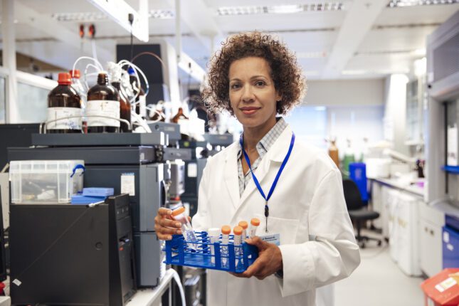 A female analyst in a lab collecting samples bottles. Used to illustrate the hidden costs of replacing lab talent.
