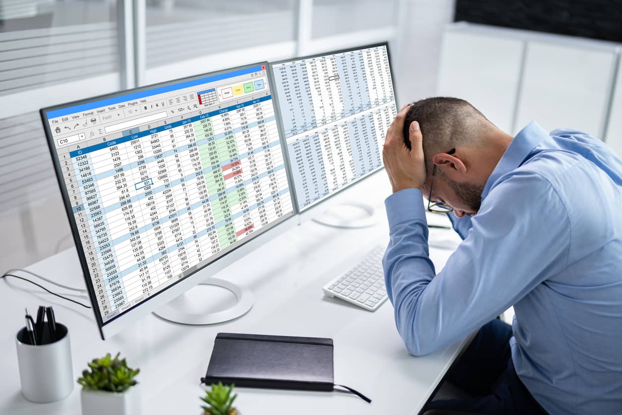 A planner cradles his head in his hands as he struggles with two screens of Excel spreadsheets, illustrating why spreadsheets are not effective resource management tools