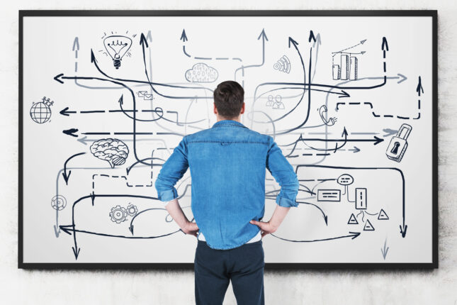 Rear view of a man looking in confusion at a whiteboard with a messy and complicated mind map on it.