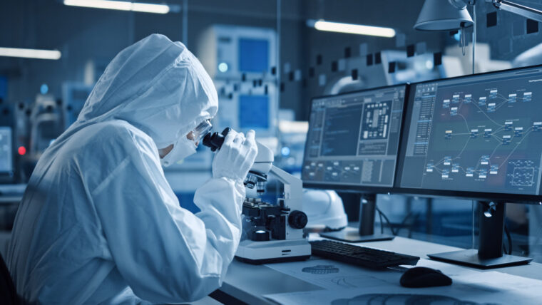 A scientist in protective clothing uses a digitally-enabled microscope to anlyze samples in a step towards a paperless future