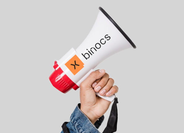 A hand holds up a megaphone empblazoned with the Binocs logo